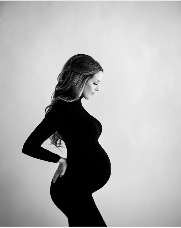 a pregnant woman poses for a black and white photo with her hands on her hips