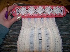 a person is holding a pink object with white yarn on it and knitting needles in the background