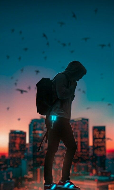 a man with a backpack standing on top of a building in the city at night