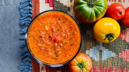 a bowl of tomato soup next to some tomatoes and peppers on a tablecloth with a blue towel