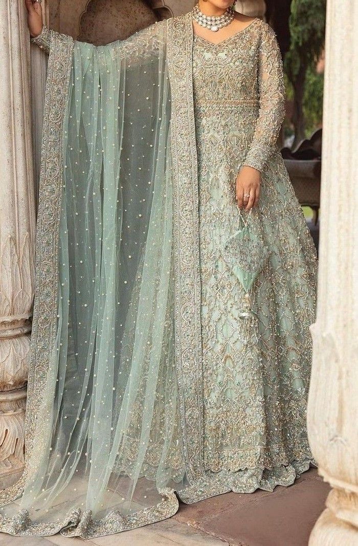 a woman standing in front of a pillar wearing a long dress with sheer sleeves and beading