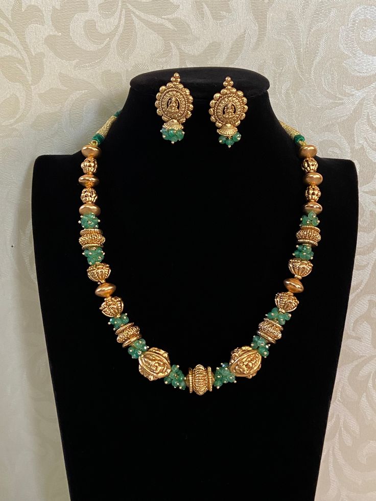 The Nakshi Balls & Green Beads Necklace is a traditional Indian jewelry piece, often inspired by ancient and classical designs These are intricately handcrafted gold beads, commonly found in traditional South Indian jewelry. Nakshi work refers to the detailed carving or embossing of figures, motifs, or patterns, often featuring floral designs, deities, or temple architecture. These gold balls are usually spherical, hollow, and exhibit high craftsmanship with a textured, antique finish. The green Bohemian Gold Bridal Necklace With Polished Beads, Gold Kundan Beaded Necklace For Puja, Gold Kundan Beaded Necklaces For Puja, Handmade Temple Jewelry Beaded Necklaces For Festivals, Temple Jewelry Handmade Beaded Necklaces For Rituals, Temple Jewelry With Gemstone Beads For Rituals, Spiritual Gemstone Beads Necklace For Festive Season, Spiritual Necklaces With Gemstone Beads For Festive Season, Gold Kundan Mala With Polished Beads