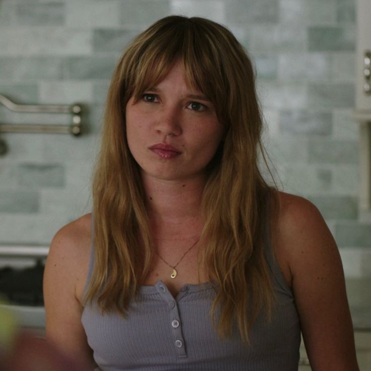 a woman with long hair standing in a kitchen looking at the camera and making a funny face