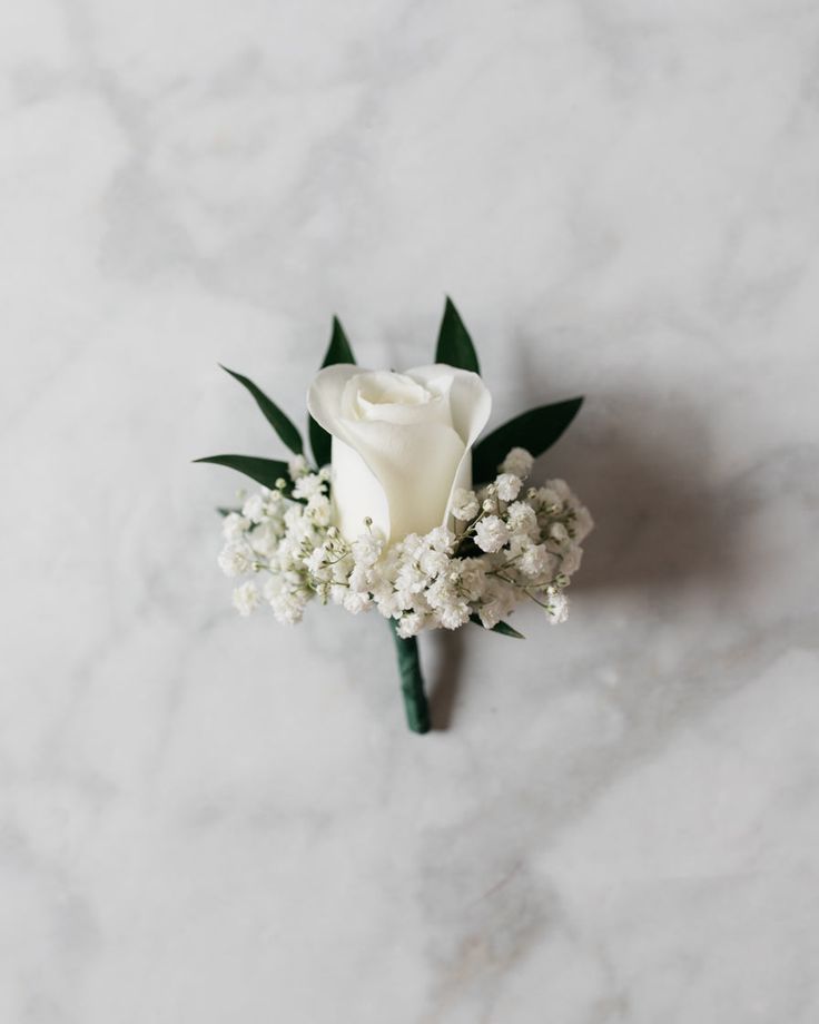 a white rose and baby's breath boutonniere on a marble surface