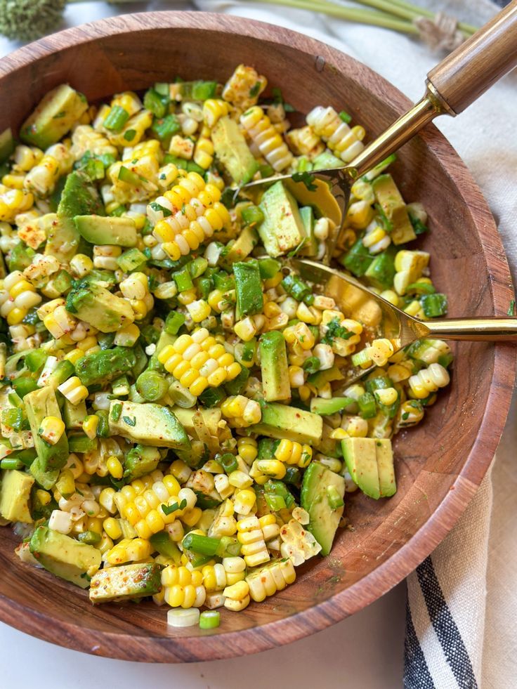 a wooden bowl filled with corn and green vegetables on top of a white table cloth