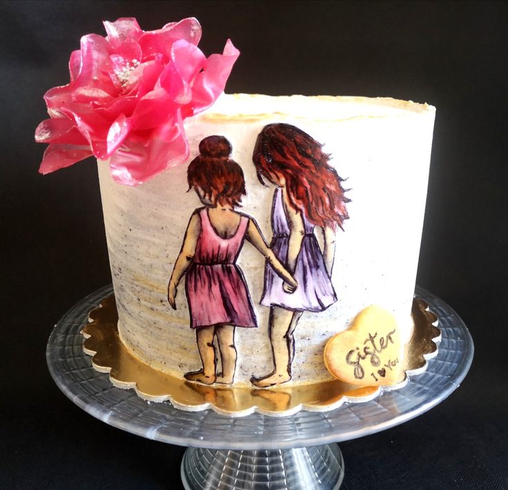 a cake decorated with two girls holding hands on top of a glass platter next to a pink flower