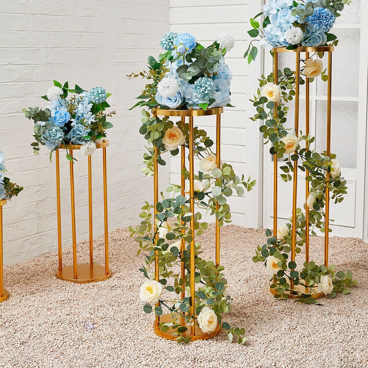 three gold vases filled with blue and white flowers on top of a carpeted floor