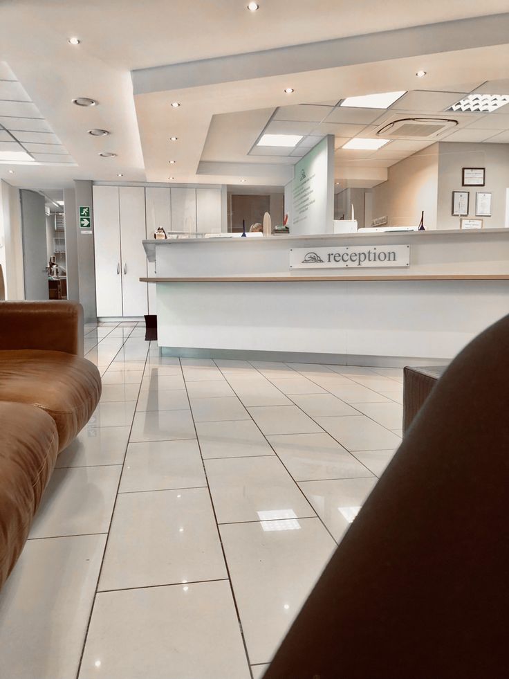 an empty lobby with white tile flooring and large reception desk in the center area