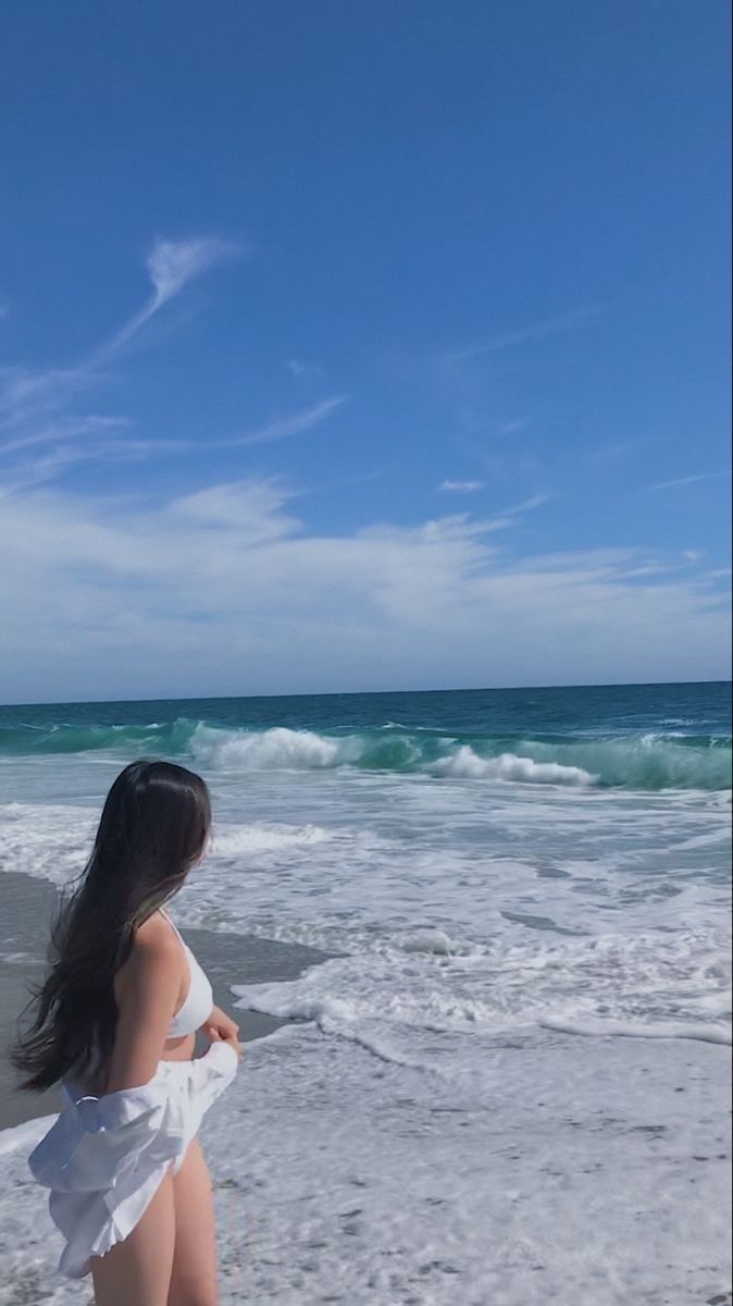 a woman standing on top of a beach next to the ocean