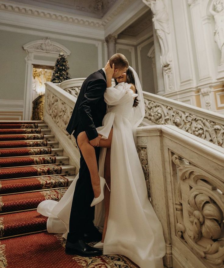 a bride and groom are kissing on the stairs at their wedding reception in an ornate building