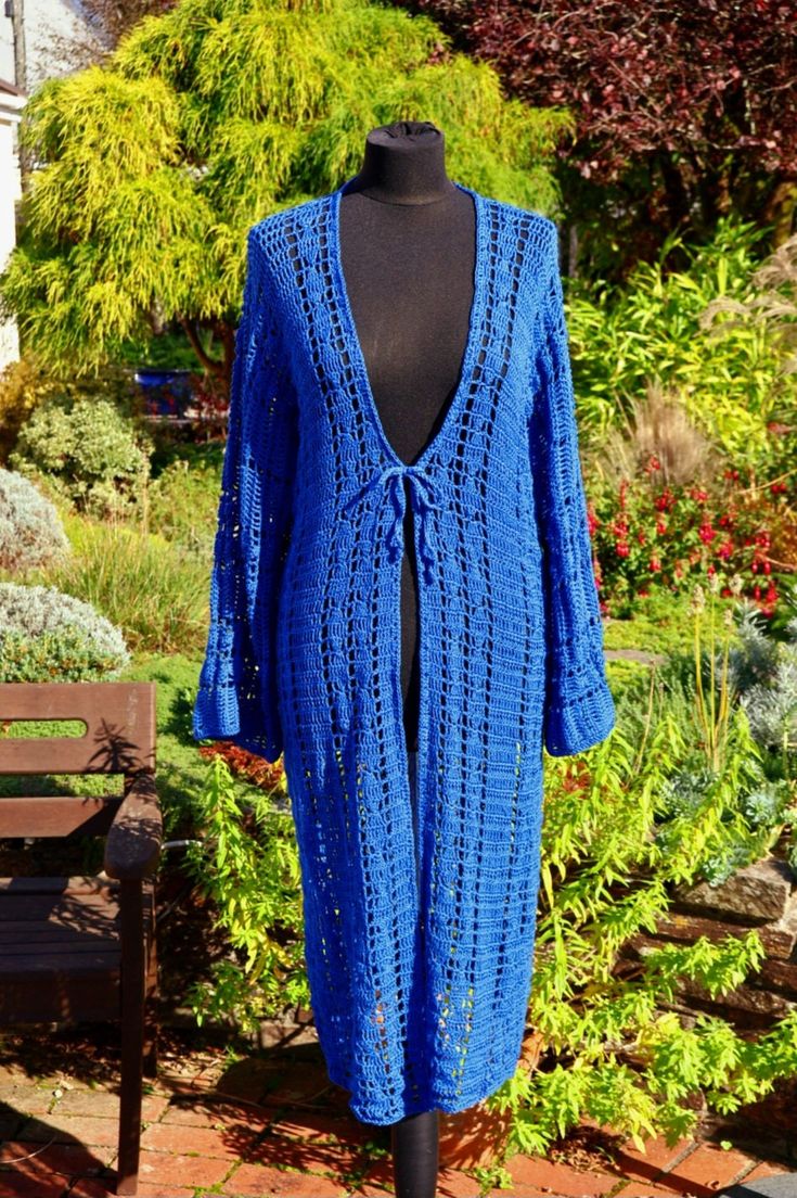 a blue crocheted cardigan on a mannequin in front of some bushes