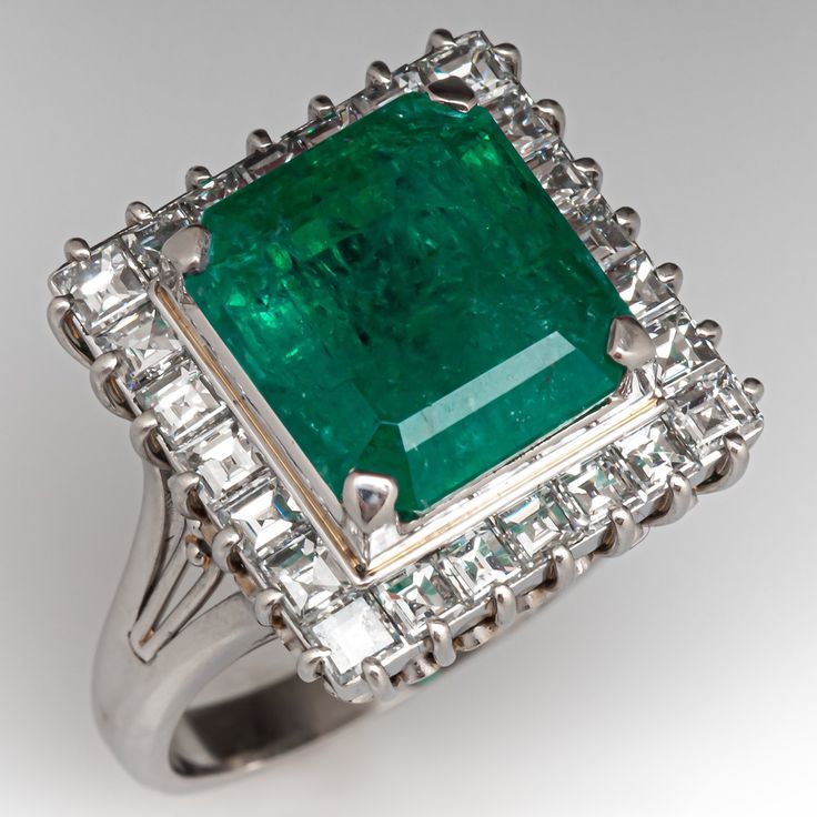 This stunning ring is centered with an emerald cut emerald, weighing 6.08 carats, in a four-prong setting. The center is surrounded by a halo, prong set with twenty-four (24) square step cut diamonds. The lower gallery features a filigree design. The ring measures 16.5mm at the top, rises 11.3mm above the finger, tapering to 2.3mm wide and 1.1mm thick at the base of the shank. It is currently a size 7.75. Formal Emerald Ring With Halo Setting, Formal Emerald Halo Ring Fine Jewelry, Emerald Halo Ring For Formal Occasions, Formal Octagon Emerald Ring With Diamond, Exquisite Emerald Ring With Halo Setting For Formal Occasions, Formal White Gold Emerald Ring With Halo, Formal Emerald Cut Emerald Ring With Halo, Gia Certified Formal Emerald Cut Emerald Ring, Timeless Formal Emerald Ring, Gia Certified