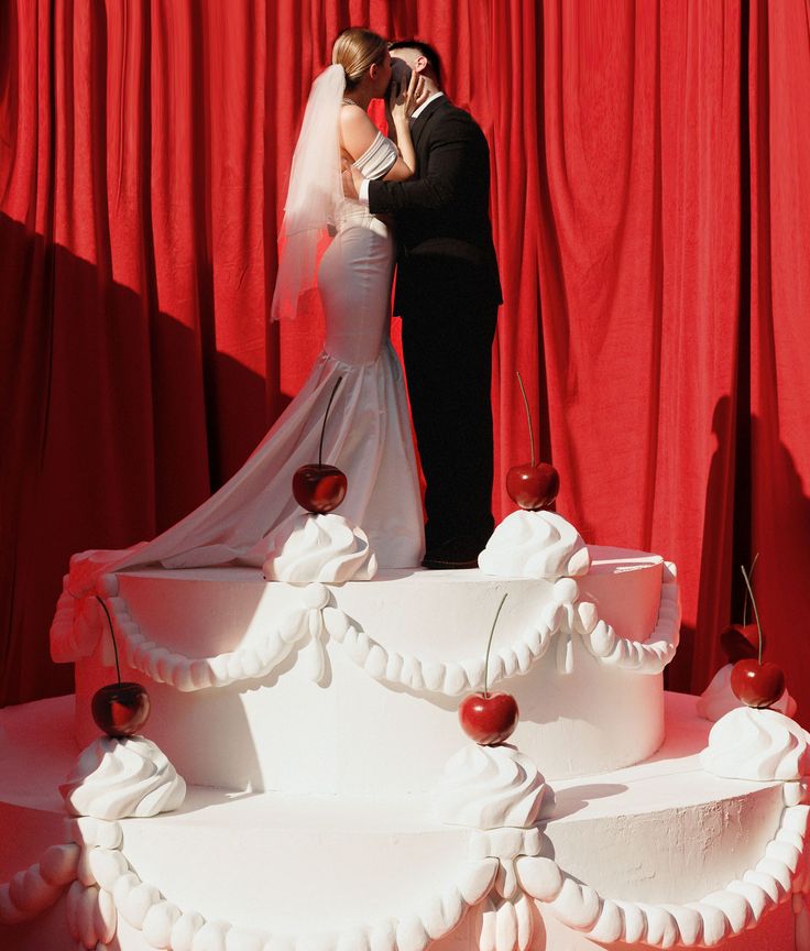 a bride and groom kissing in front of a wedding cake with red curtains behind them