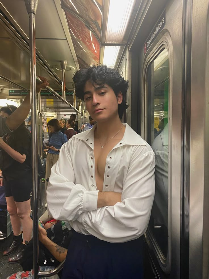 a man in white shirt and blue shorts standing on subway train with his arms crossed