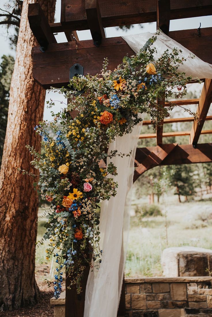 a wedding arch with flowers and greenery hanging from it's sides in front of a tree