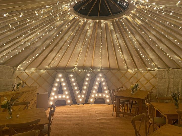 the inside of a yurt with lights on it's ceiling and wooden tables