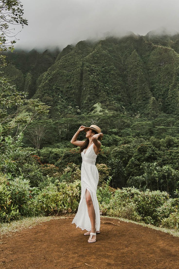 a woman in a white dress standing on top of a dirt field next to trees