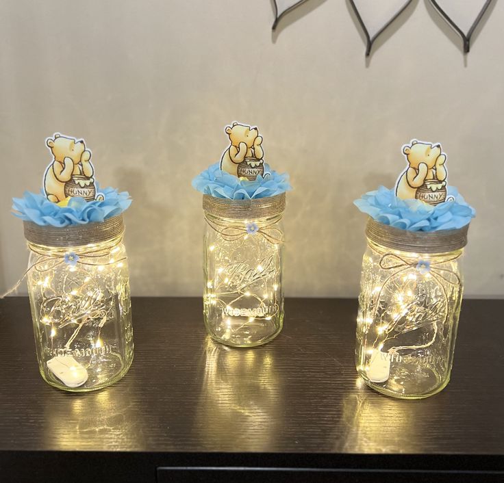 three mason jars with teddy bears in them on a wooden table next to a clock