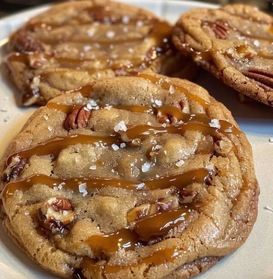 three cookies with pecans and caramel drizzled on them sitting on a white plate