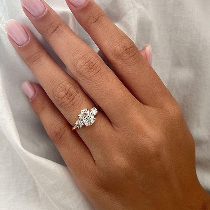 a woman's hand with a three stone ring on her left and the middle finger