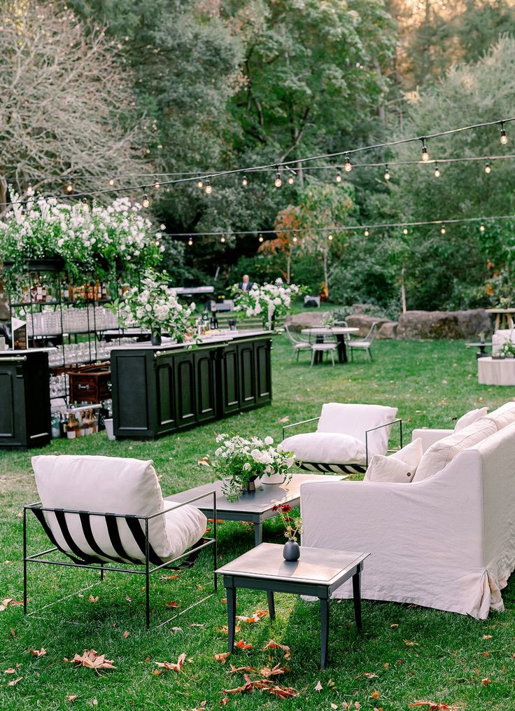 an outdoor seating area with chairs, tables and flowers on the grass in front of trees