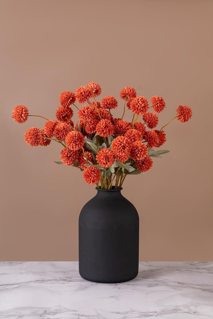 a black vase filled with orange flowers on top of a table