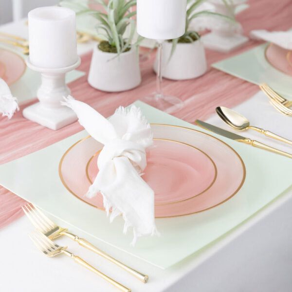 the table is set with pink and white plates, gold cutlery, and candles