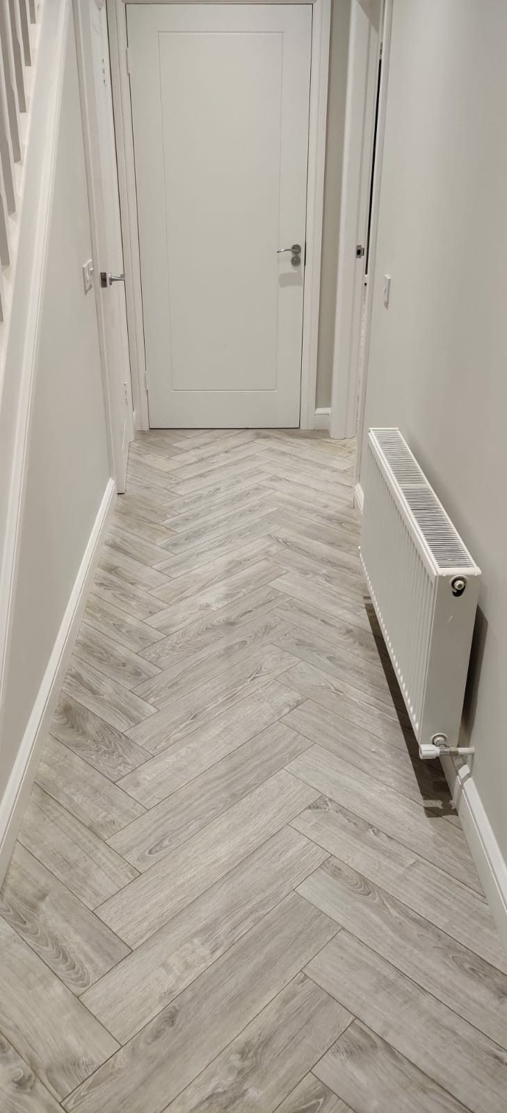 an empty hallway with wood flooring and white painted walls, along with a radiator