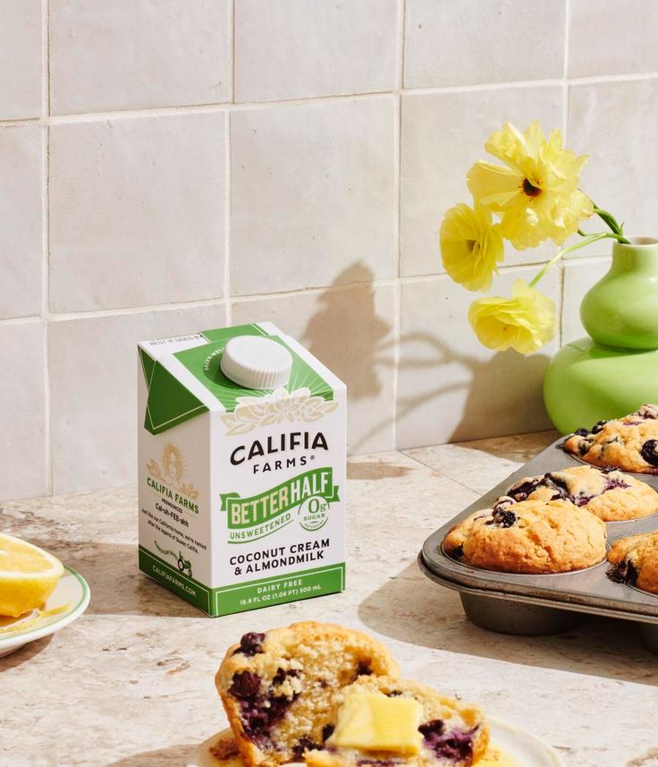 some blueberry muffins are sitting on a counter next to a carton of buttermilk