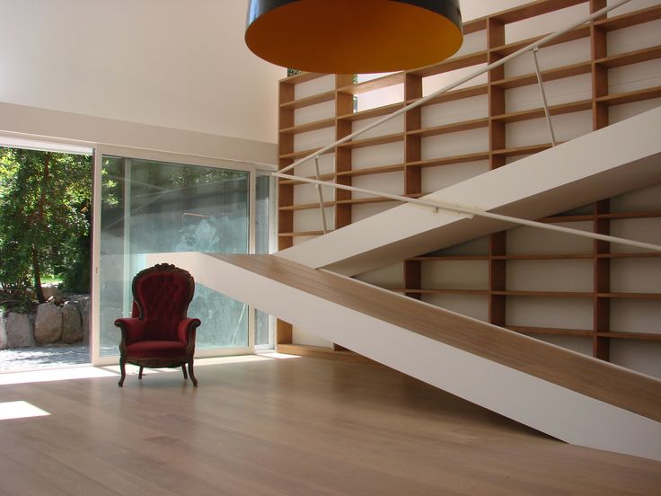 a red chair sitting in front of a wooden stair case next to a large window