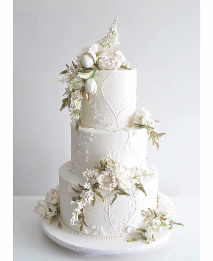 a three tiered white wedding cake with flowers on it's sides and leaves