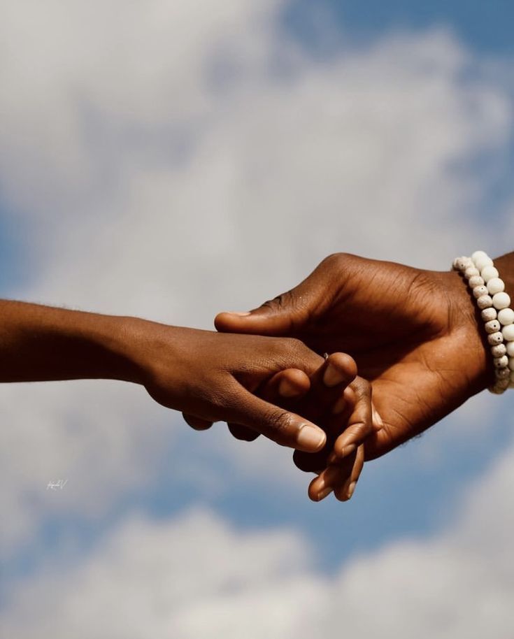 two hands holding each other with sky in the background