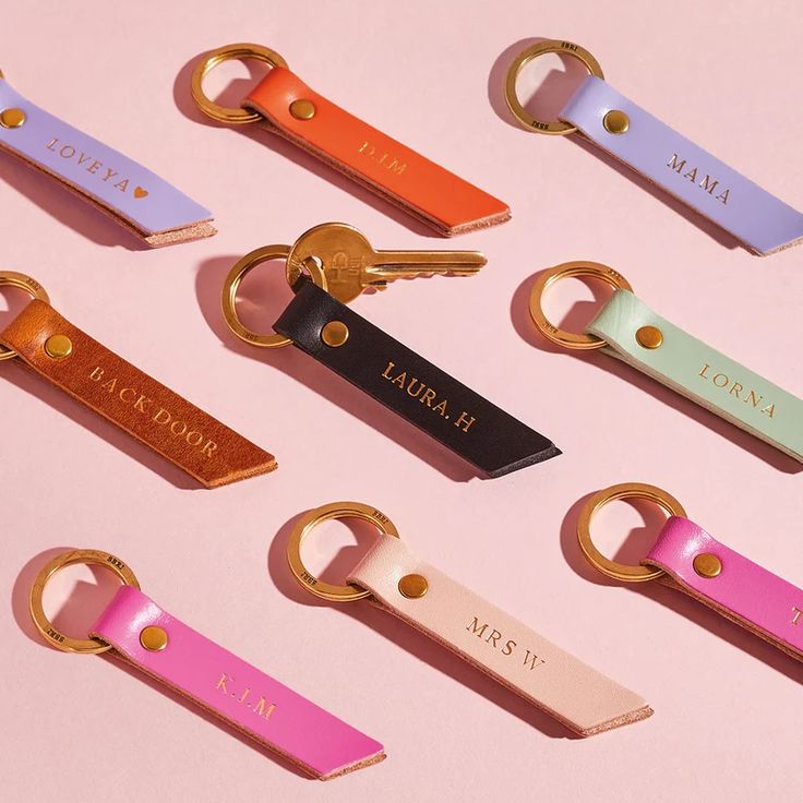 six different colored keychains with personalized tags attached to them on a pink surface