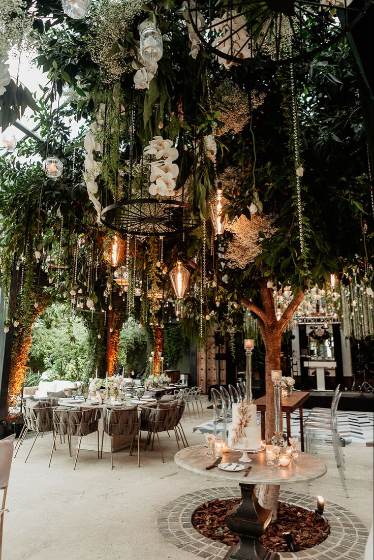 an indoor wedding venue with tables, chairs and flowers hanging from the ceiling above them