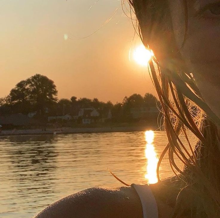 the sun is setting behind a woman's head in front of a body of water