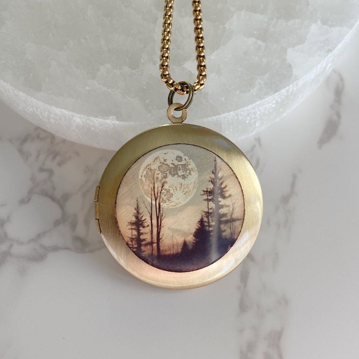 "Now offering custom engraving.  Visit shop for details. Introducing my Gold Full Moon Forest Photo Locket that will make a perfect addition to your jewelry collection. Crafted from high-quality gold plated brass, this locket features a forest with a large full moon hanging in the sky above. Measuring 32mm in diameter, it opens to reveal a secret compartment where you can keep pictures, messages, or any small memento that holds a special meaning to you. The image on the locket is an art print pe Spiritual Round Pendant Jewelry With Engraving Option, Oval Moon Phase Necklace As A Gift, Moon Phase Oval Necklace For Gifts, Spiritual Medallion Jewelry With Engraving Option, Oval Moon Phase Necklace Gift, Oval Moon Phase Necklace For Gift, Spiritual Medallion Jewelry For Personalized Gift, Celestial Style Locket Jewelry Gift, Celestial Locket Necklace For Gifts