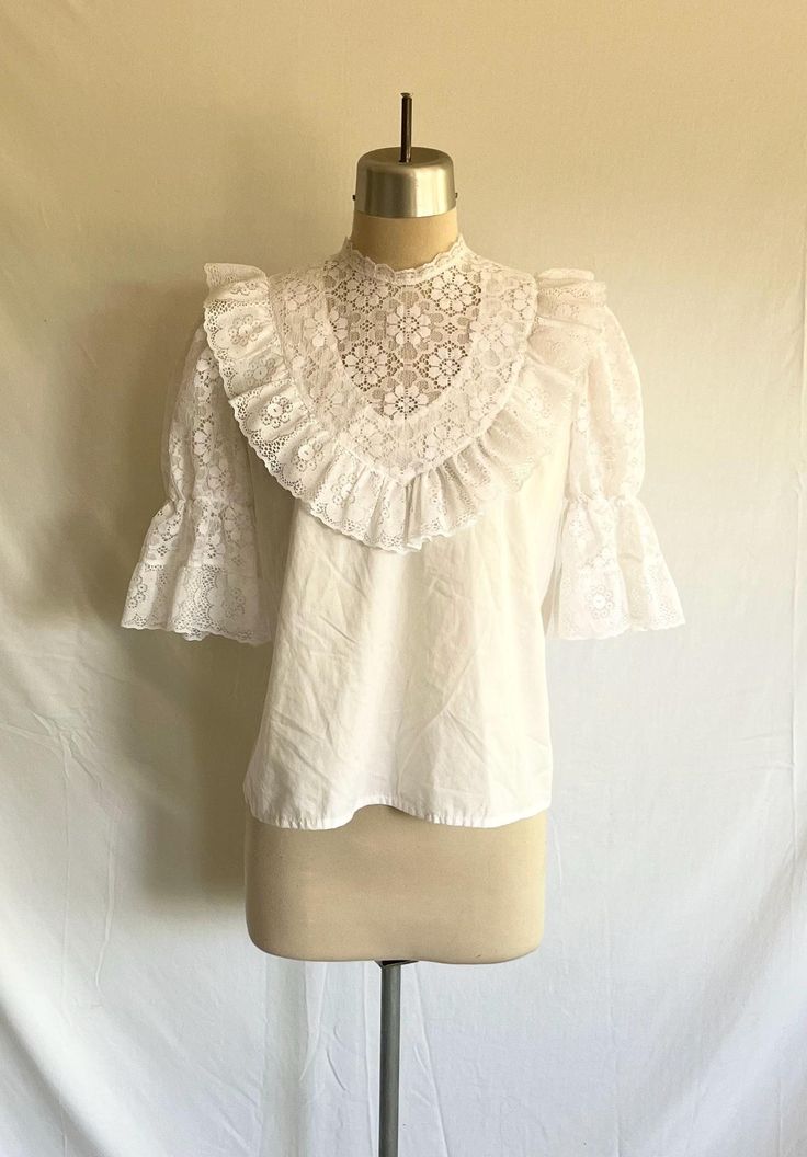 Beautiful 1980's Victorian style lace puff sleeve blouse featuring a semi sheer yoke, lace trimmed crew neck and ruffles! Solid part of blouse is a white cotton blend. The rest of the blouse is a floral nylon lace.  Blouse zips up the back with a plastic zipper. Blouse is clean and in excellent condition!  Label:  Kate Schorer - Colorado Springs, CO - Made in USA - S Measurements: would best fit a modern size S/M Bust= 38 1/2" Bottom opening= 42" Shoulder width= 13 1/2" Sleeve length= 13" Bicep= 18" Sleeve opening= 8" relaxed, stretches to 14" Body length from side neck down to hem edge= 23" White Victorian Blouse, Bohemian Broderie Anglaise Short Sleeve Blouse, Bohemian Blouse With Broderie Anglaise Short Sleeves, Vintage Lace Trim Tops, Vintage Spring Tops With Lace Trim, Vintage Blouse With Lace Sleeves, Vintage Lace Trim Tops For Spring, Vintage Fashion Lace Trim Tops For Spring, Spring Vintage Lace Top With Lace Trim