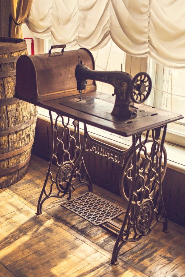 an old fashioned sewing machine sitting on top of a wooden table next to a window