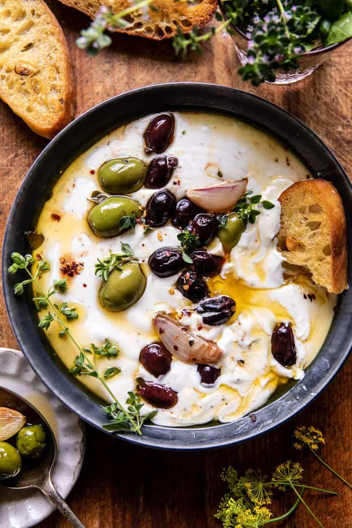 a bowl filled with olives, sour cream and bread on top of a wooden table