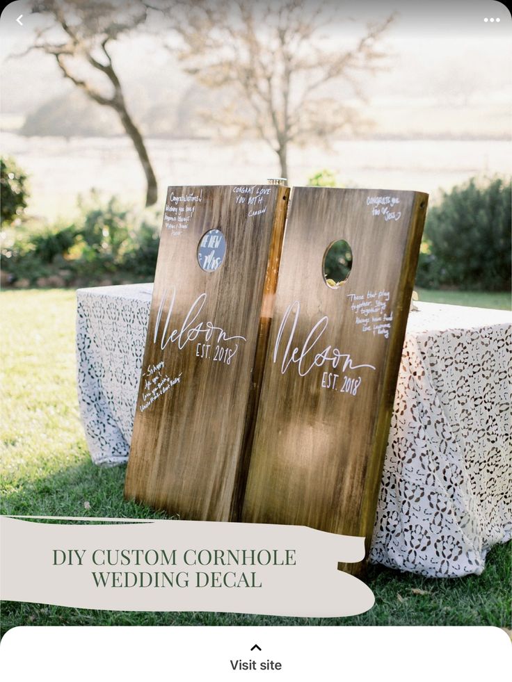 two wooden cornhole game boards sitting on top of a lush green field next to a white table cloth