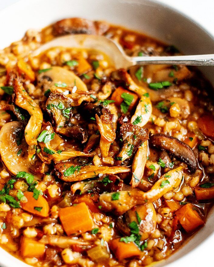 a white bowl filled with stew and vegetables on top of a wooden table next to a spoon