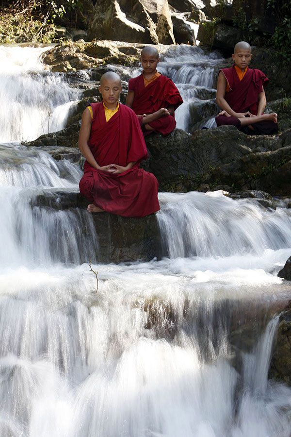 three monks are sitting on rocks in front of a waterfall with water cascading down it