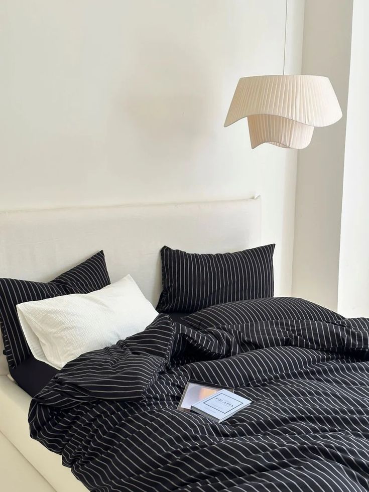 a bed with black and white striped comforter next to a lamp on the wall