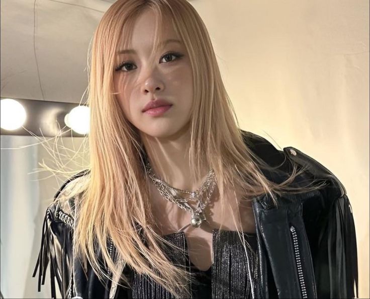 a woman with long blonde hair wearing a black leather jacket and silver chain around her neck