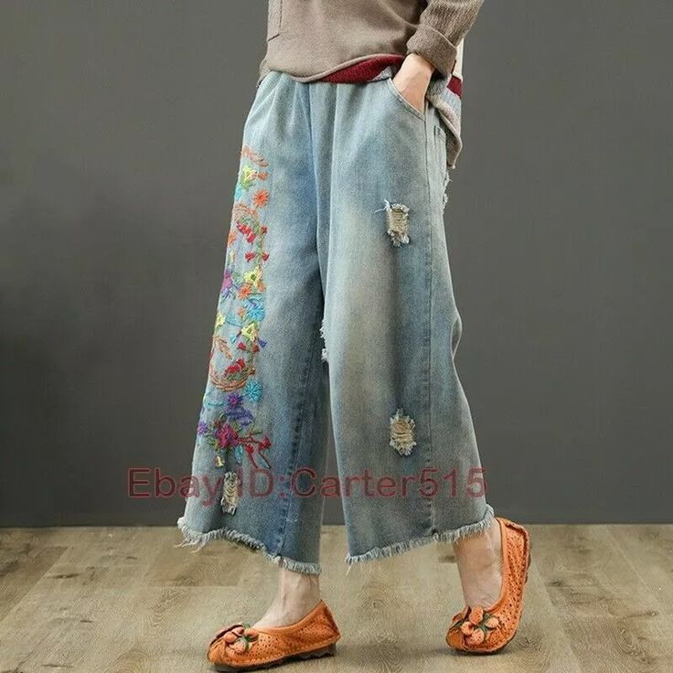 a woman standing on top of a wooden floor wearing blue jeans with flowers painted on them