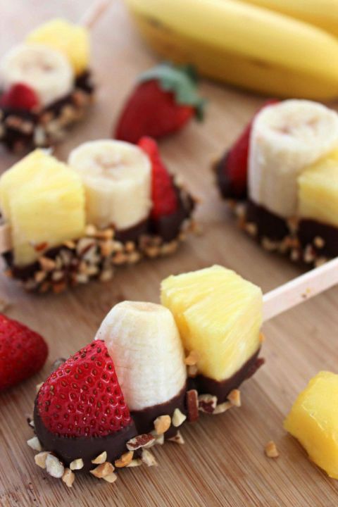 chocolate covered strawberries, bananas and pineapples are arranged on a cutting board