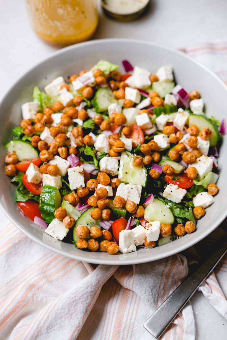 a salad with chickpeas, cucumbers and red onions in a white bowl