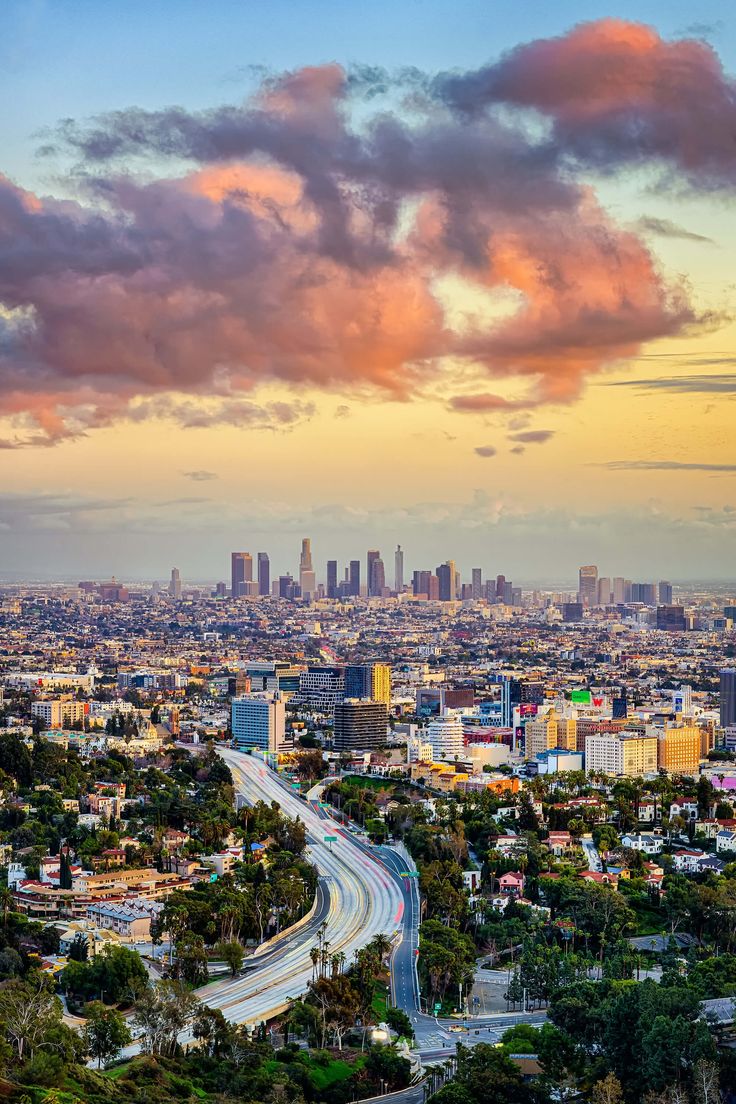 an aerial view of a city with tall buildings and clouds in the sky at sunset