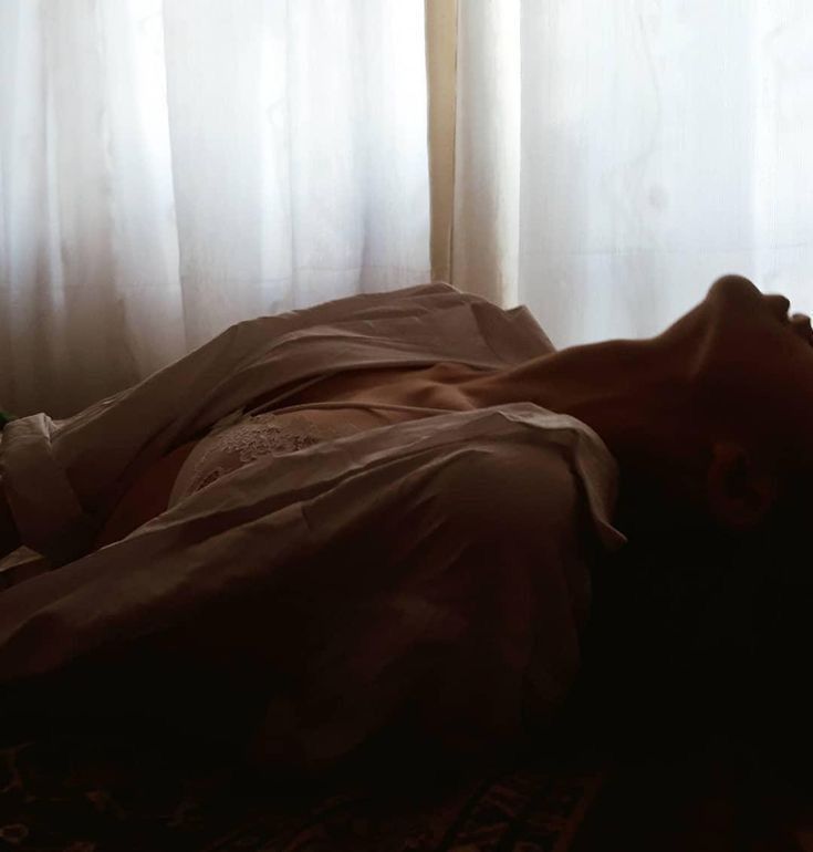 a person is laying down on the floor in front of a window with white curtains