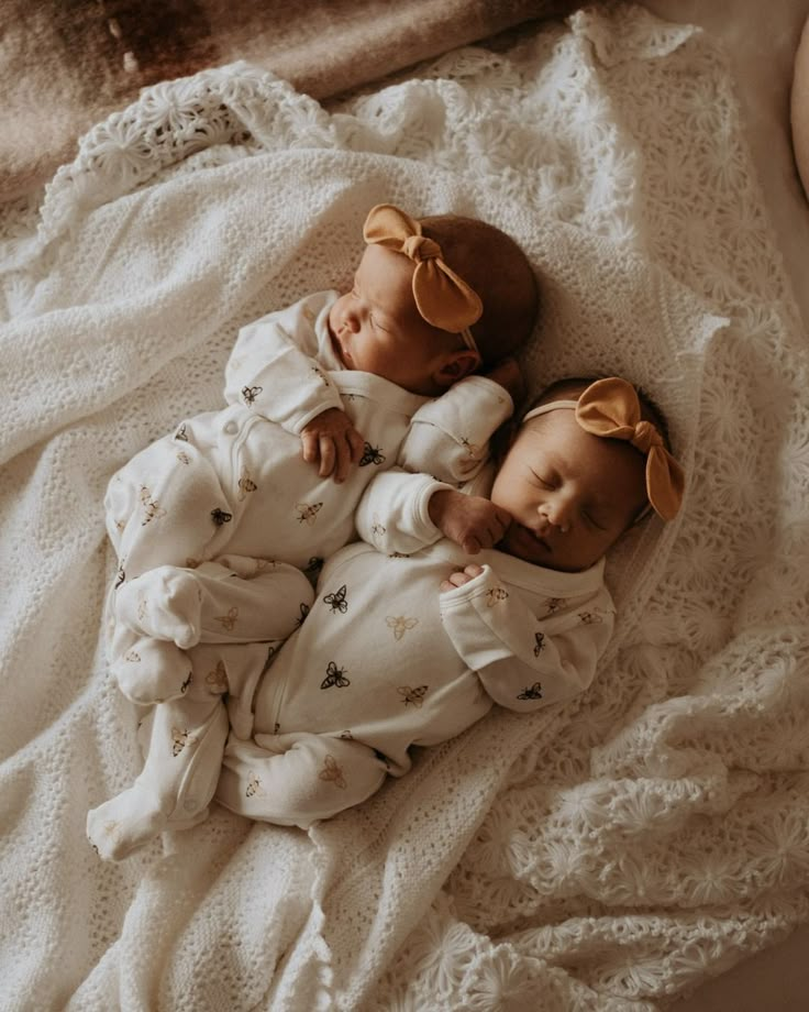 two baby dolls laying on top of a white blanket